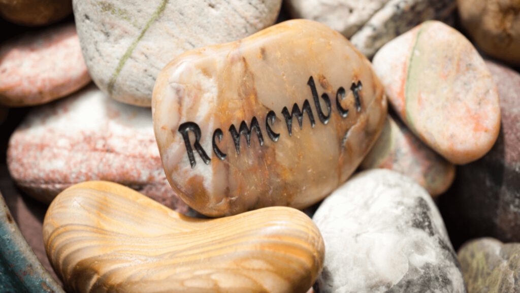 a collection of polished stones, one in the middle with an etching that says Remember