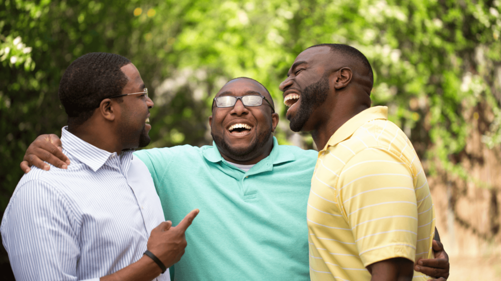 Three Black men in pastel shirts standing close together and laughing