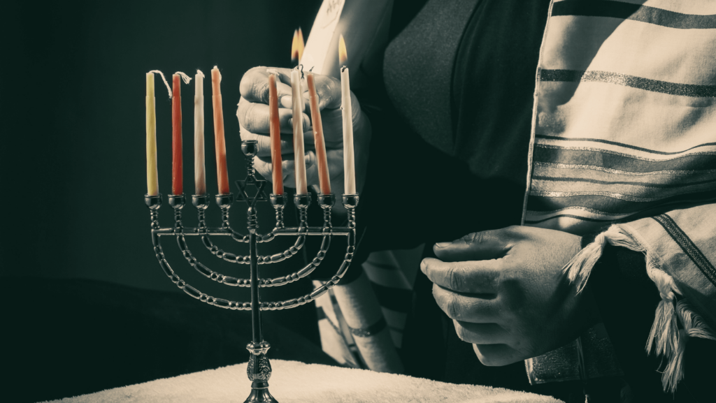 Close-up of someone wearing a talit lighting the menorah