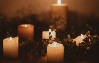 Lit candles surrounded by greenery, creating a warm and cozy atmosphere in soft, dim lighting.
