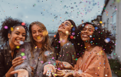 Four people smiling outdoors, surrounded by colorful confetti in the air.
