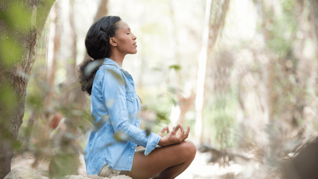 A Black woman in a blue dress meditating outdoors
