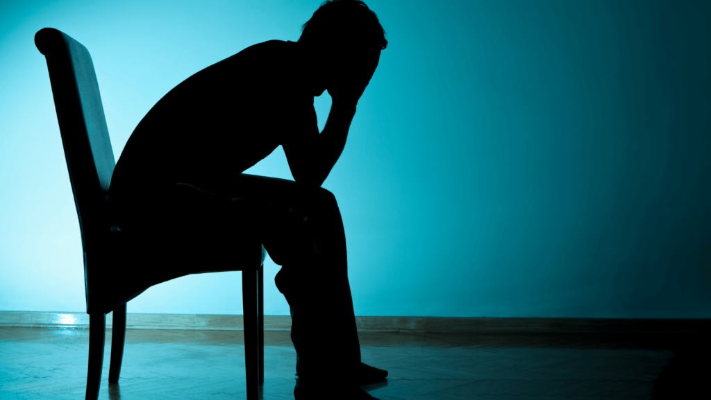 Silhouette in blue light of a person bent over in a chair