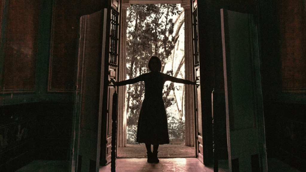A silhouetted woman in a dress opening double doors into the outdoors.