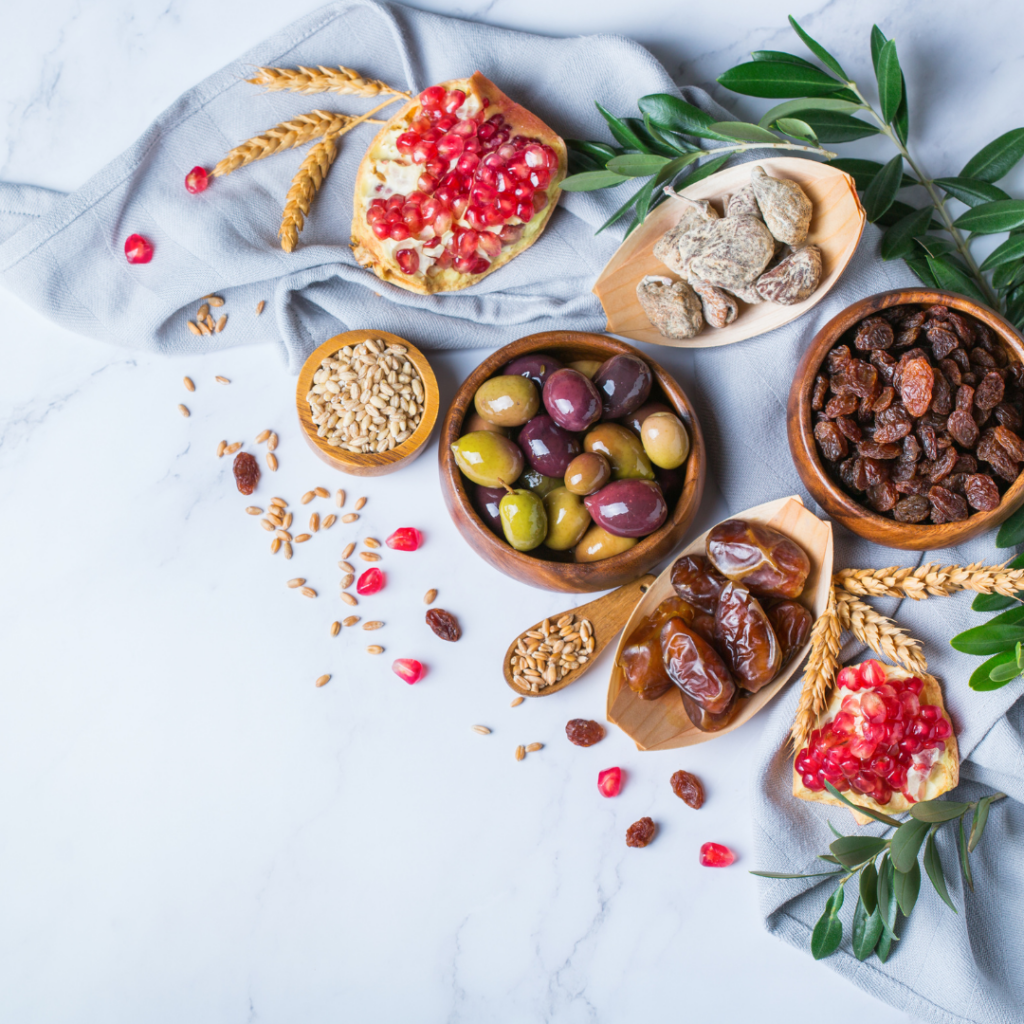 Assorted Mediterranean snacks with olives, dates, nuts, raisins, and pomegranate on a marble surface.