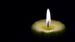 A single lit candle glows softly in the dark, with light illuminating the wax around the flame.