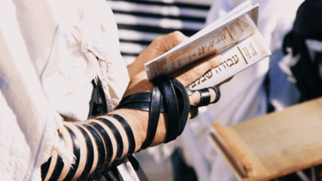 Close-up of a person with tefillin wrapped around their arm holding a prayer book.