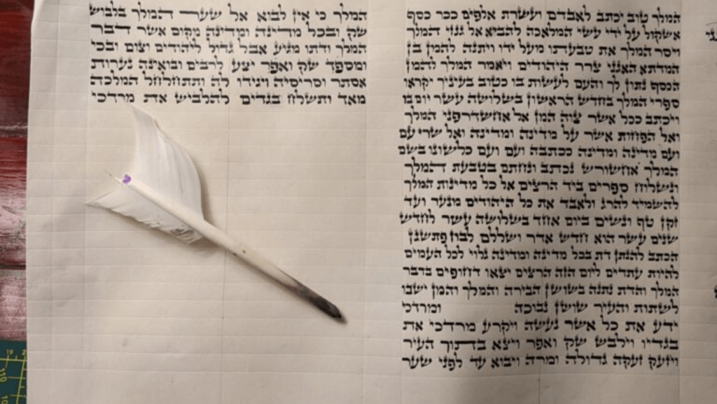 A piece of paper with handwritten Hebrew script on it and a quill pen