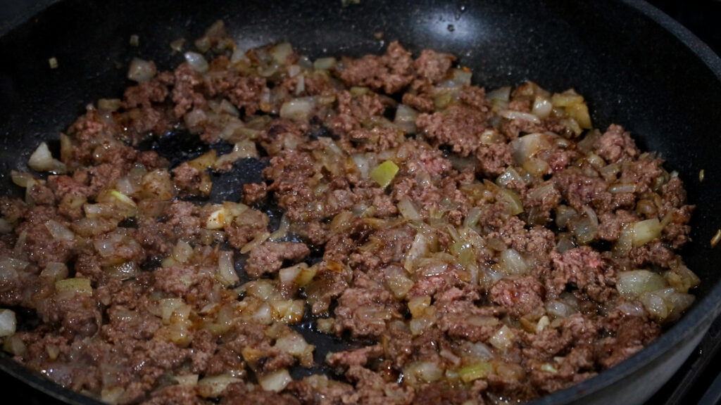 Ground beef and diced onions cooking in a skillet.