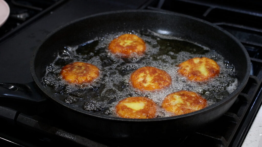 Six golden patties frying in bubbling oil on a black pan.