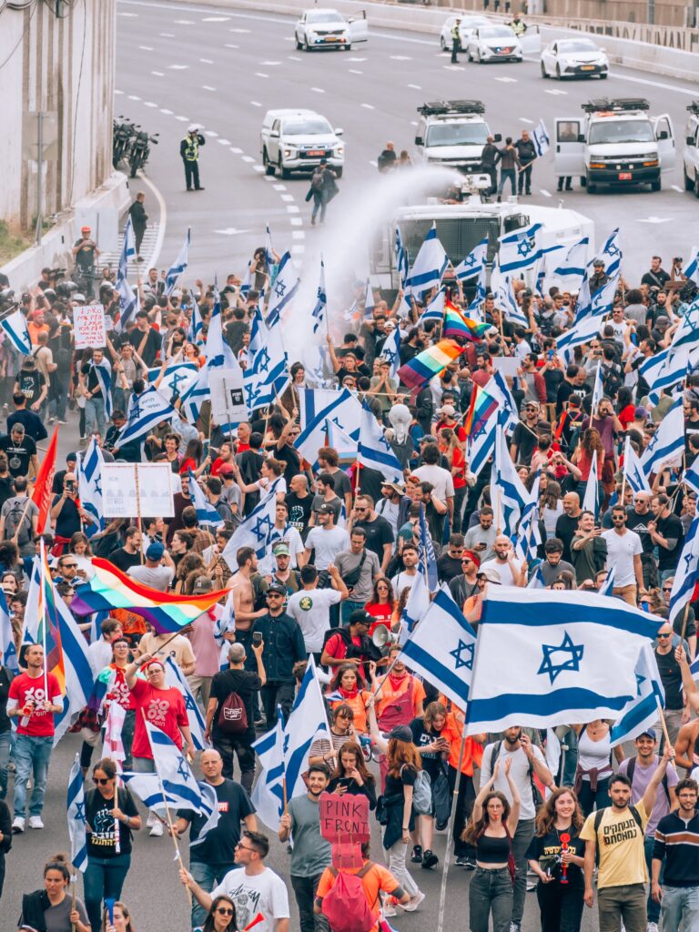 A protest with people holding Israeli flags and signs, marching on a road.