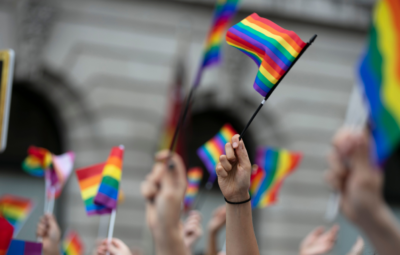 People holding rainbow flags at a parade, with a blurred building in the background.