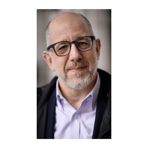 A bald man with glasses, a beard, and a smile, wearing a light purple shirt and a dark jacket.