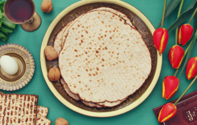 A Passover Seder plate with matzo, walnuts, egg, wine, tulips, and a book on a turquoise table.
