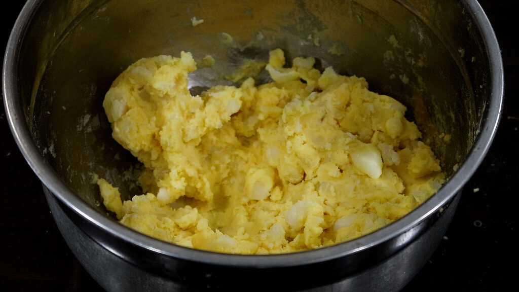 Bowl of mashed potatoes with small chunks in a metal bowl.