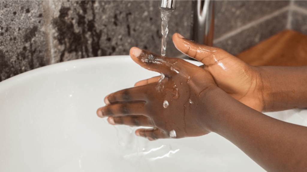 close-up of a Black person washing their hands in a white sink.