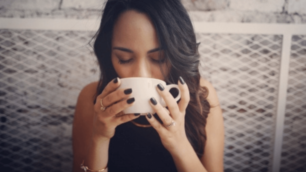 A woman with long dark hair drinks coffee from a white mug