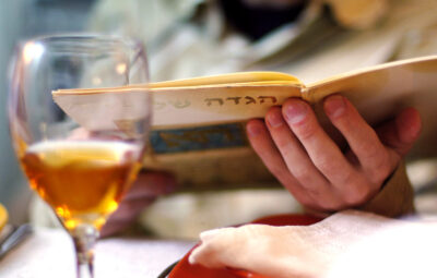 Person holding an open book, next to a half-full wine glass on a table.