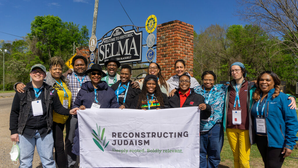 A group of people posing with a Reconstructing Judaism banner in front of a Welcome to Selma sign.