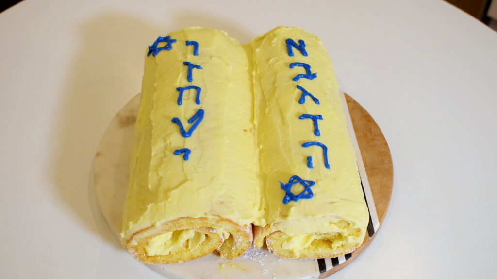 Two yellow rolled cakes designed like Torah scrolls, with blue Hebrew letters and Star of David decorations.