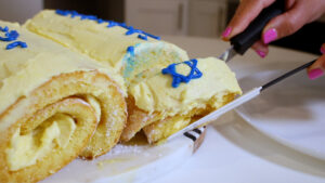 A person slices a cake with yellow frosting and blue star decorations on a white plate.