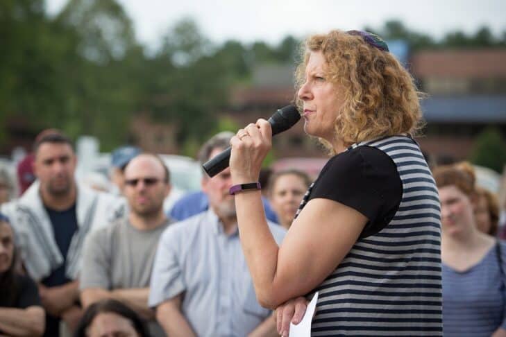Holding a mic, Rabbi Barbara Penzner addresses a crowd outdoors