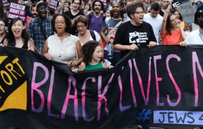 A diverse group holds a Black Lives Matter banner during a protest, displaying signs and chanting.