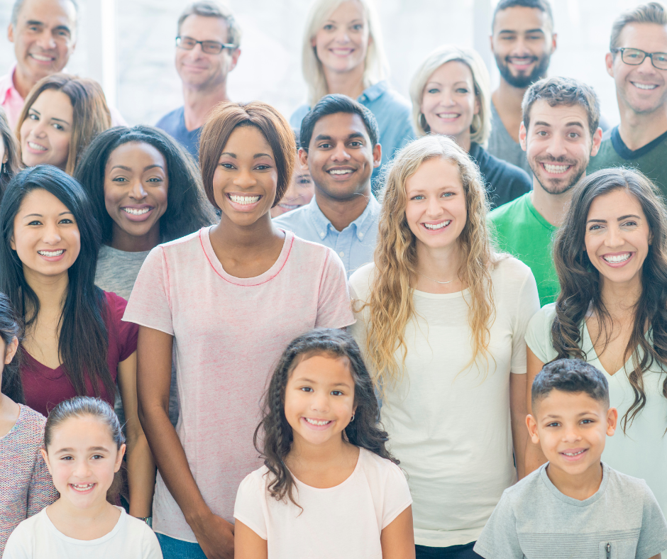 A diverse group of smiling people, including adults and children, standing together for a group photo.
