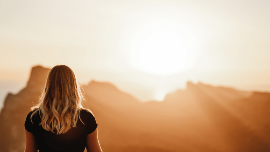 A woman with blonde hair looking at a mountain range at sunrise