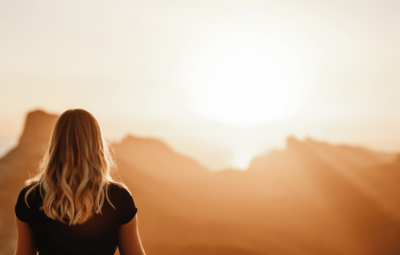 A woman with blonde hair looking at a mountain range at sunrise