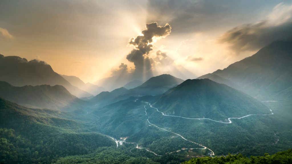 The sun shining through clouds over green mountains