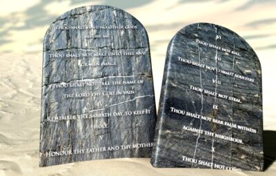 Two stone tablets with the Ten Commandments inscribed, set on a sandy surface.