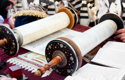 Open Torah scrolls on a table, surrounded by people wearing traditional garments.