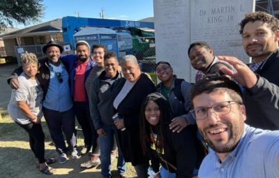 A diverse group of people smiling and posing together outdoors near a monument.