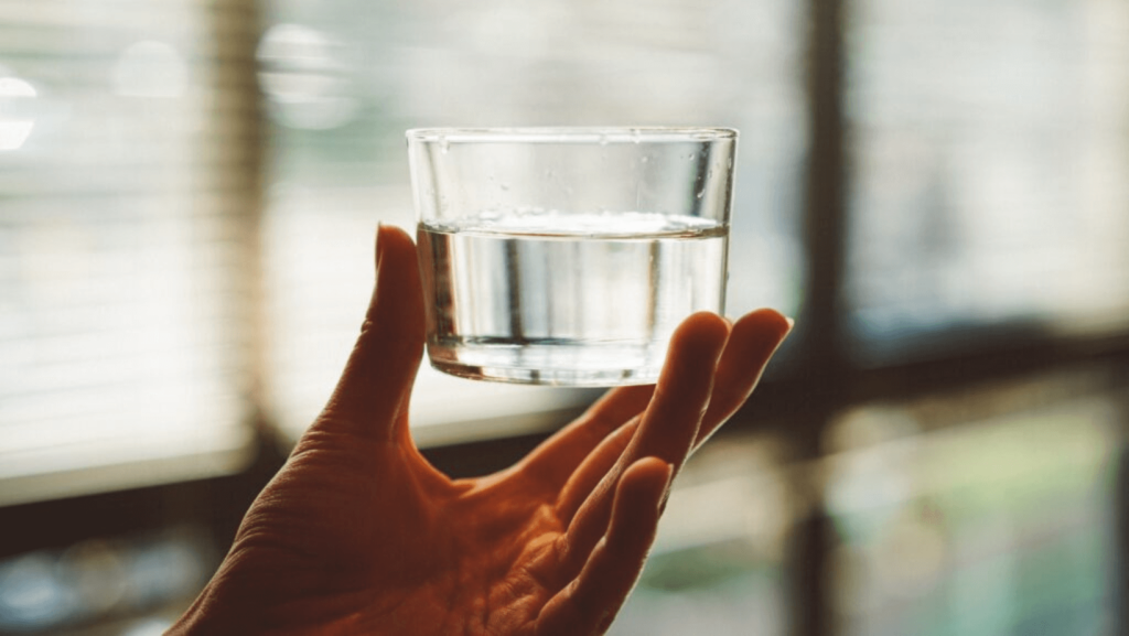 A hand holding a shallow glass cup of water.