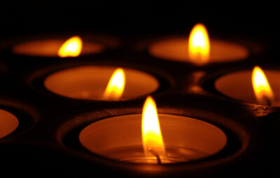 Close-up of several lit candles glowing warmly in the dark.