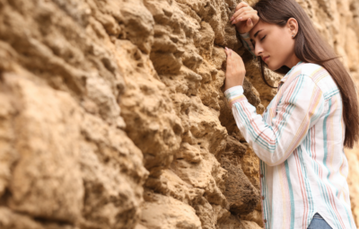 Woman in striped shirt leans against a textured stone wall, eyes closed, appearing contemplative.