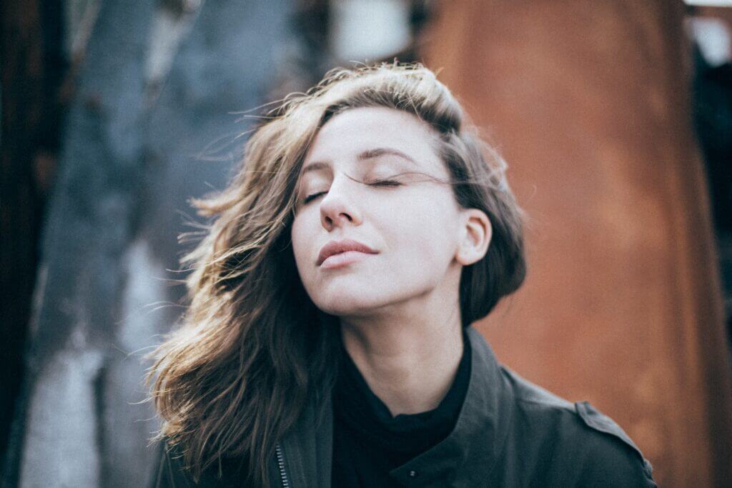 White woman with long brown hair with her eyes closed against an abstract background