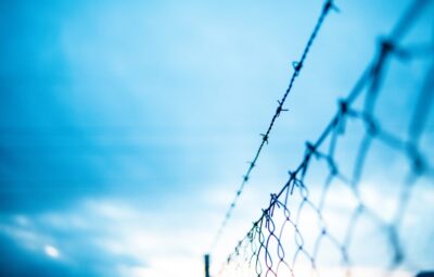 Close-up of a barbed wire fence against a blurred blue sky background.