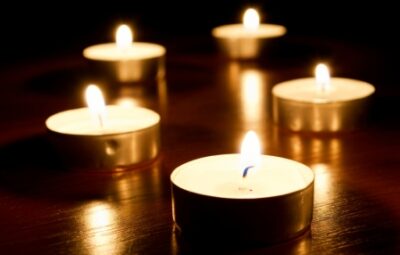 Five lit tealight candles on a dark wooden surface, casting a warm glow.