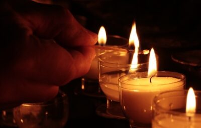 A hand lighting multiple small candles in a dark setting, creating a warm glow.
