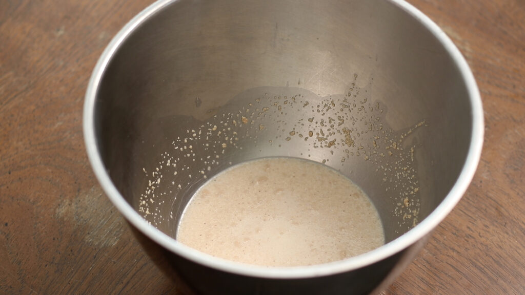A metal bowl with yeast mixture soaking in water on a wooden surface.