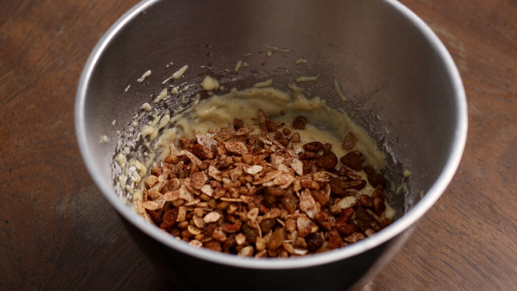 A mixing bowl with batter and crushed nuts on a wooden table.