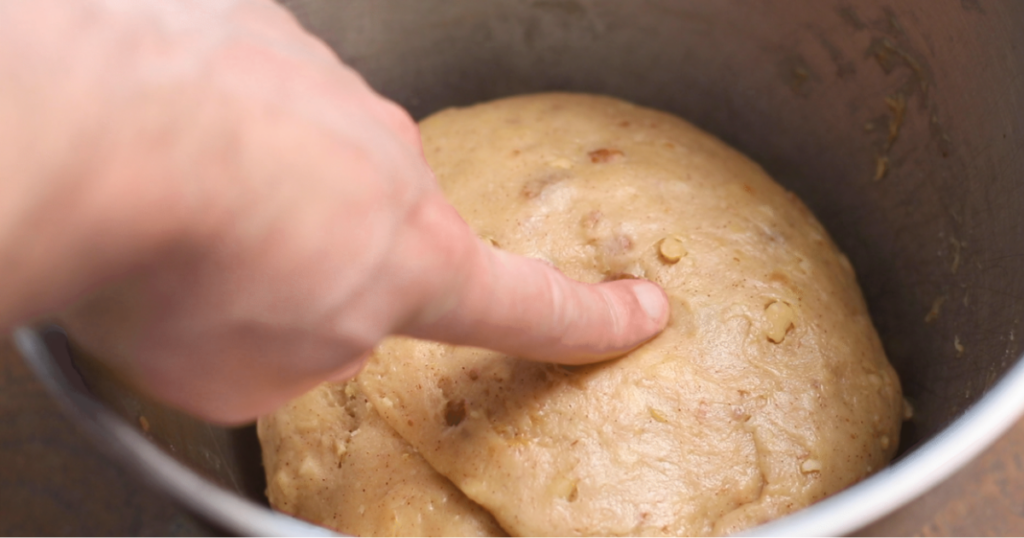 A hand pokes a ball of dough resting in a metal bowl.