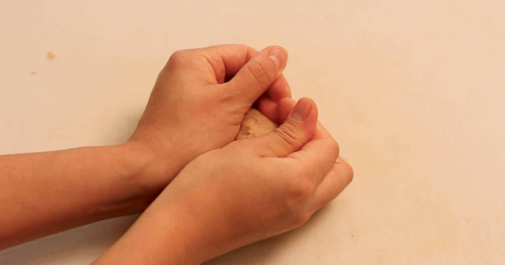 Hands kneading dough on a light surface.
