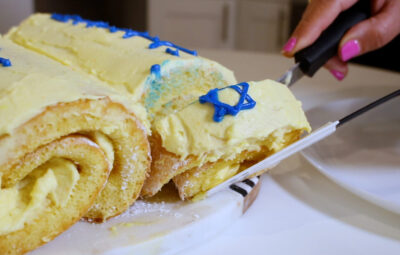 Person slicing a yellow cream roll cake with blue star decorations on top.