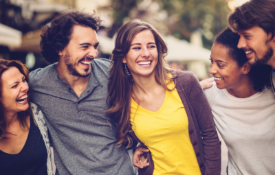 Group of friends laughing and embracing outdoors on a sunny day.