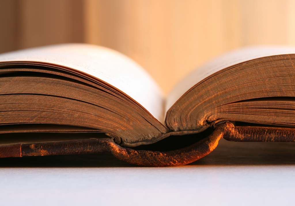 An open book with yellowed pages, viewed from the bottom edge, against a warm, soft-focus background.