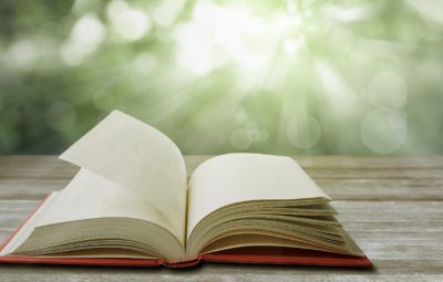 Open book on a wooden table with sunlight and bokeh in the background.