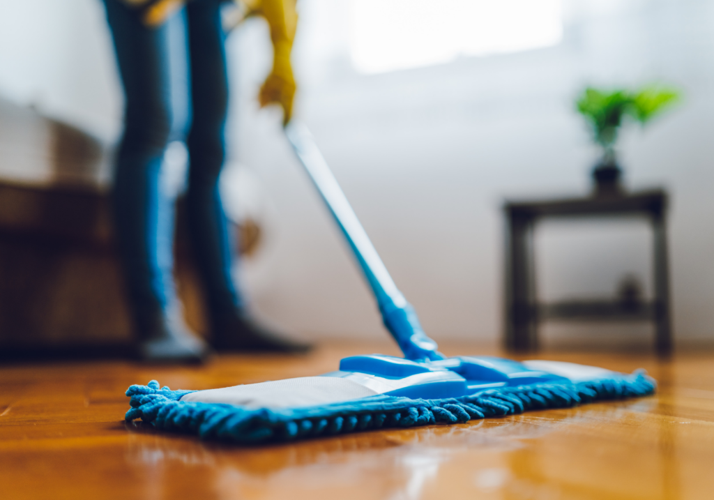 Person mopping a wooden floor with a blue mop in a bright room.